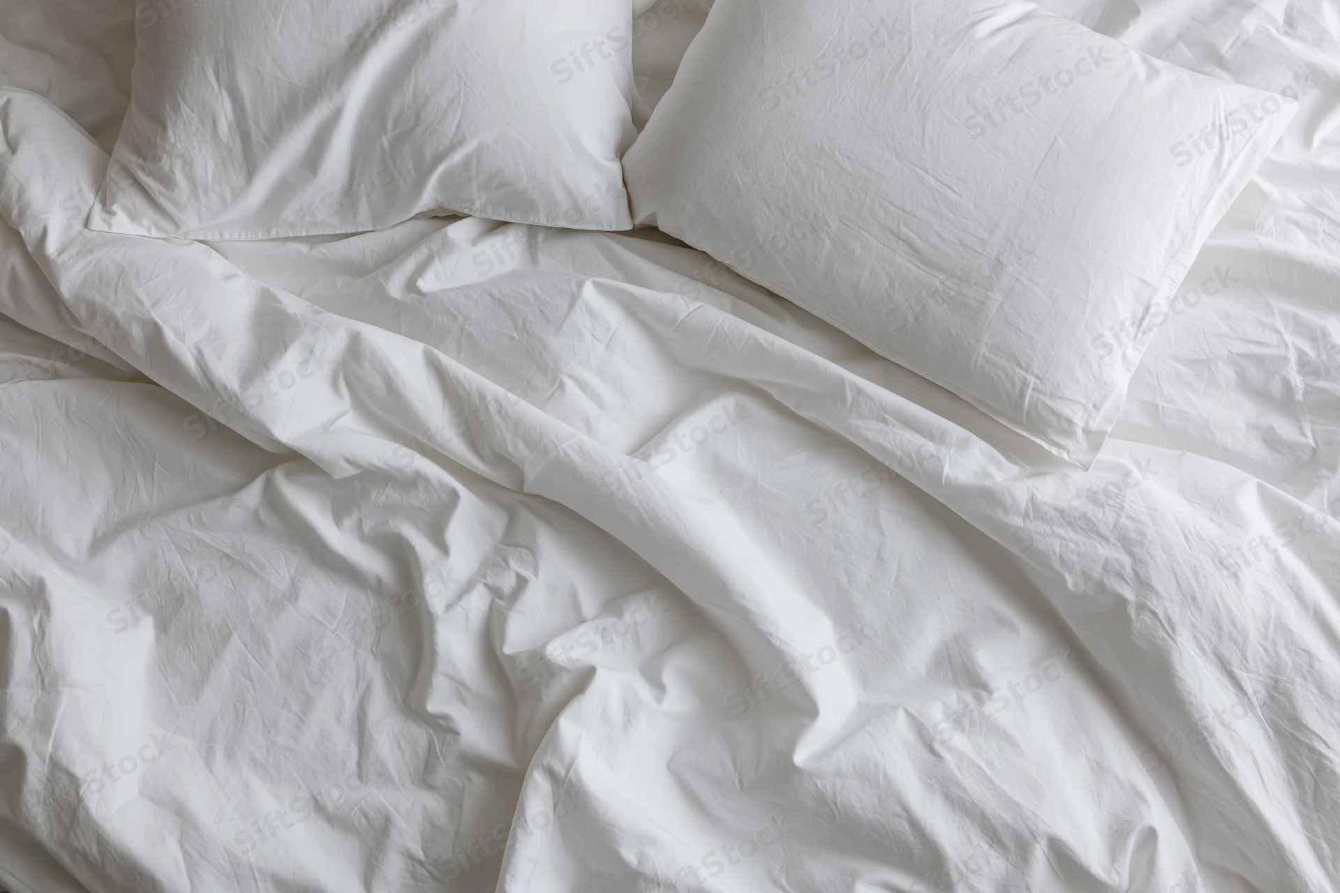 Unmade bed with crumpled white cotton sheets and two rumpled pillows viewed from above