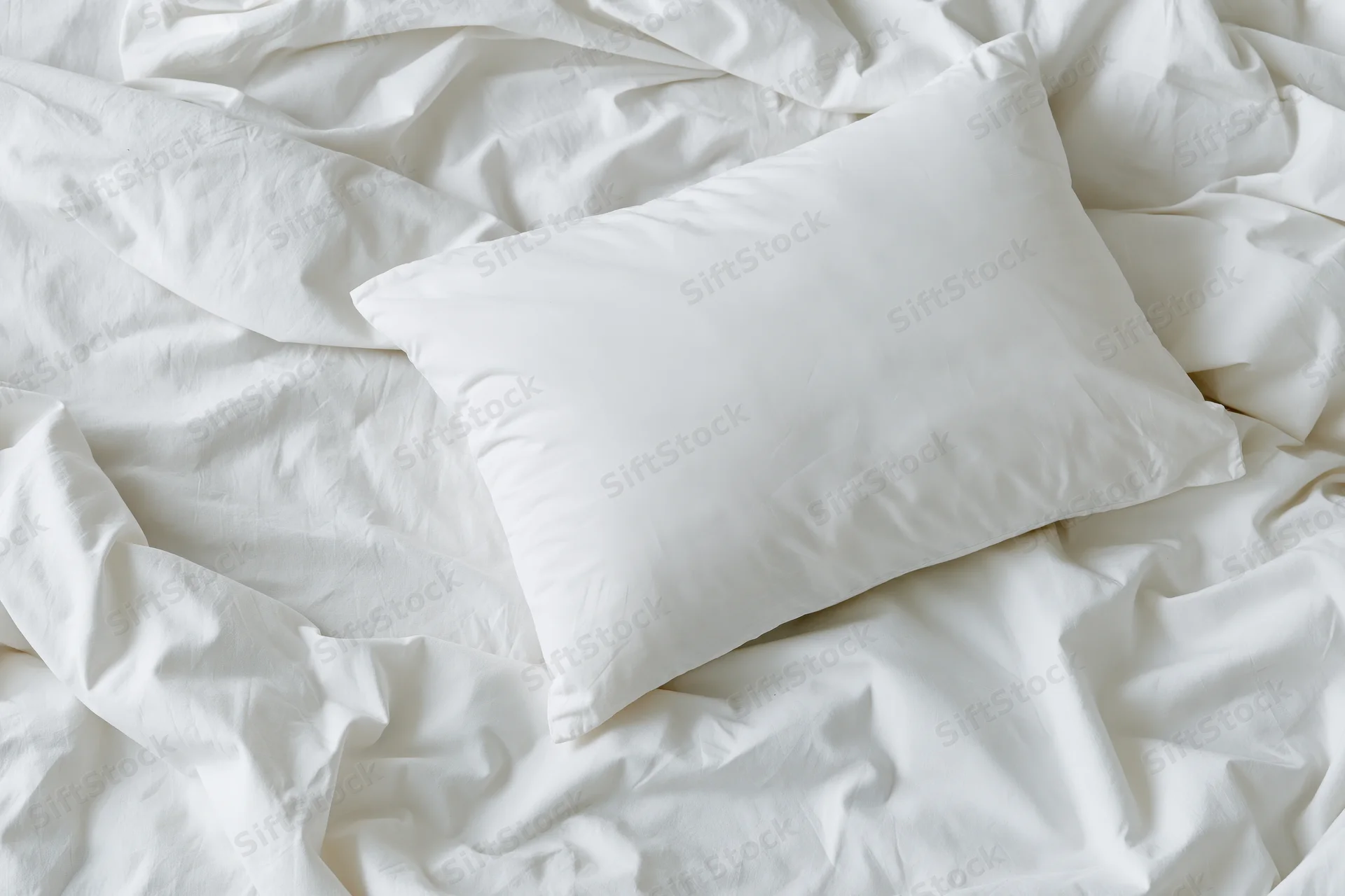 White pillow resting on rumpled white sheets in unmade bed