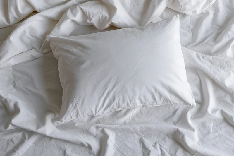 White pillow resting on crumpled white sheets in an unmade bed