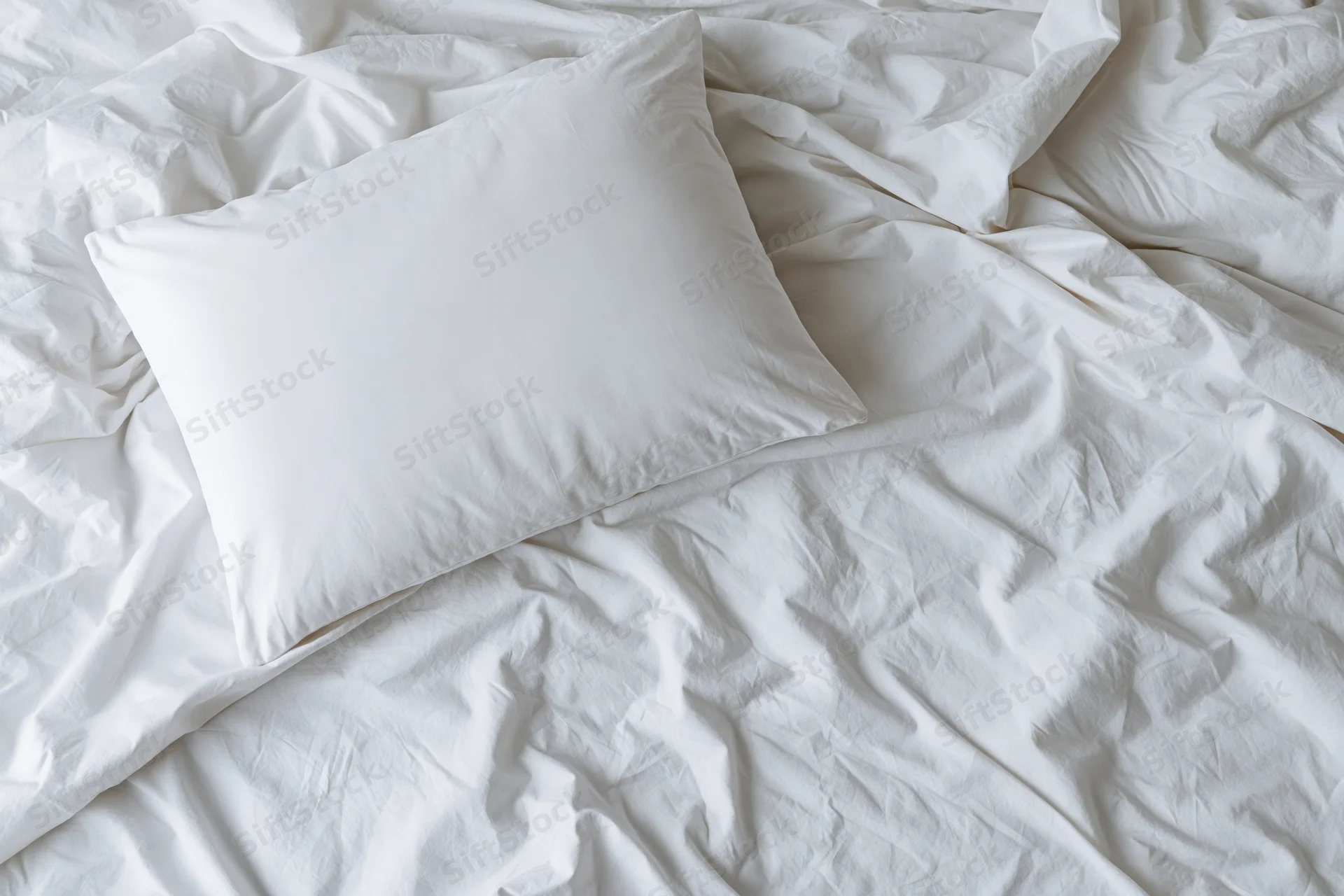Unmade bed with a white pillow resting on wrinkled white sheets in a bedroom