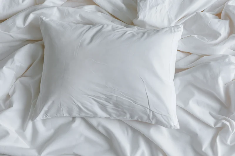 White pillow resting on crumpled white sheets in unmade bed