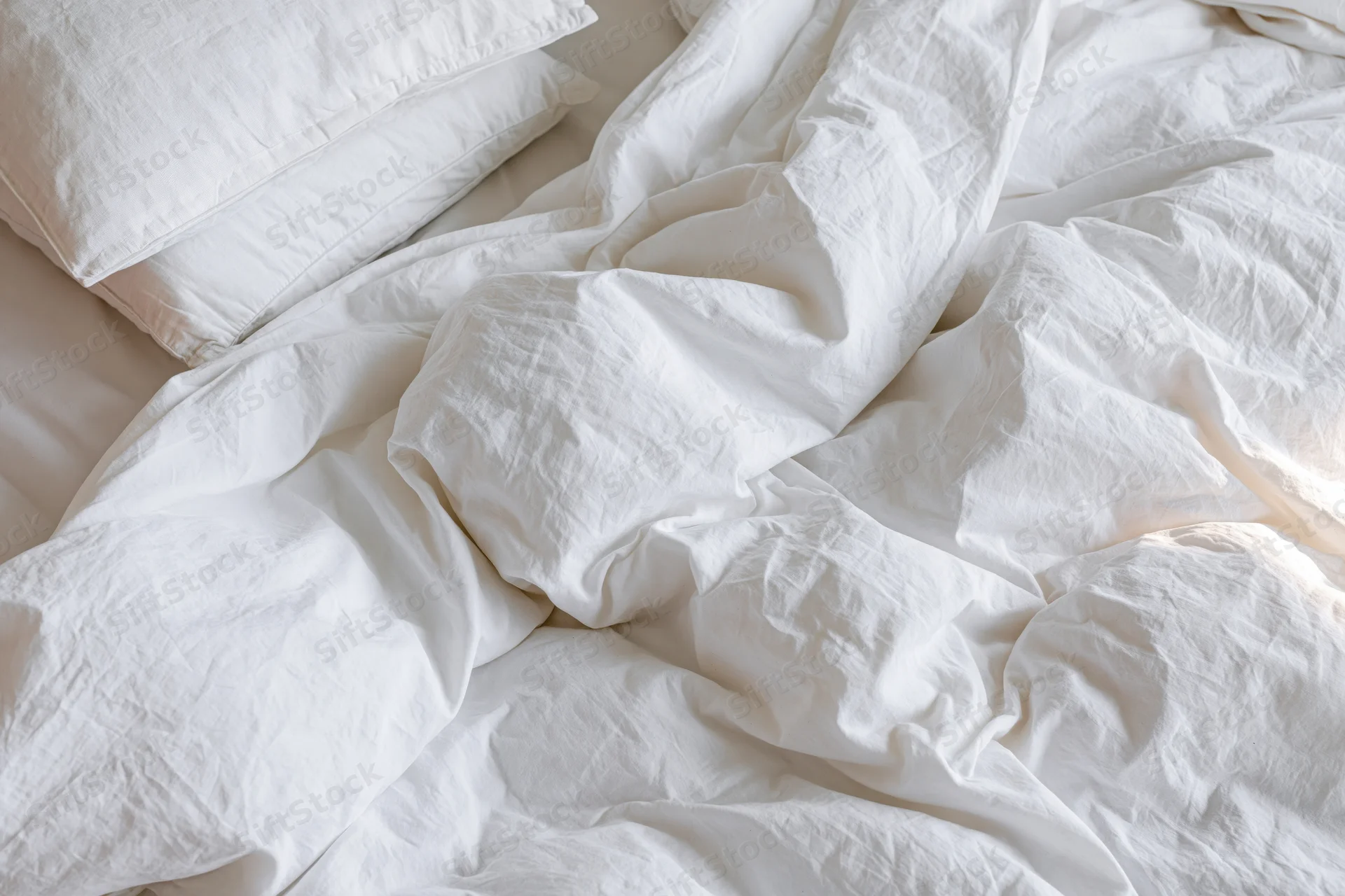 Unmade bed with rumpled white cotton duvet and two pillows in bedroom