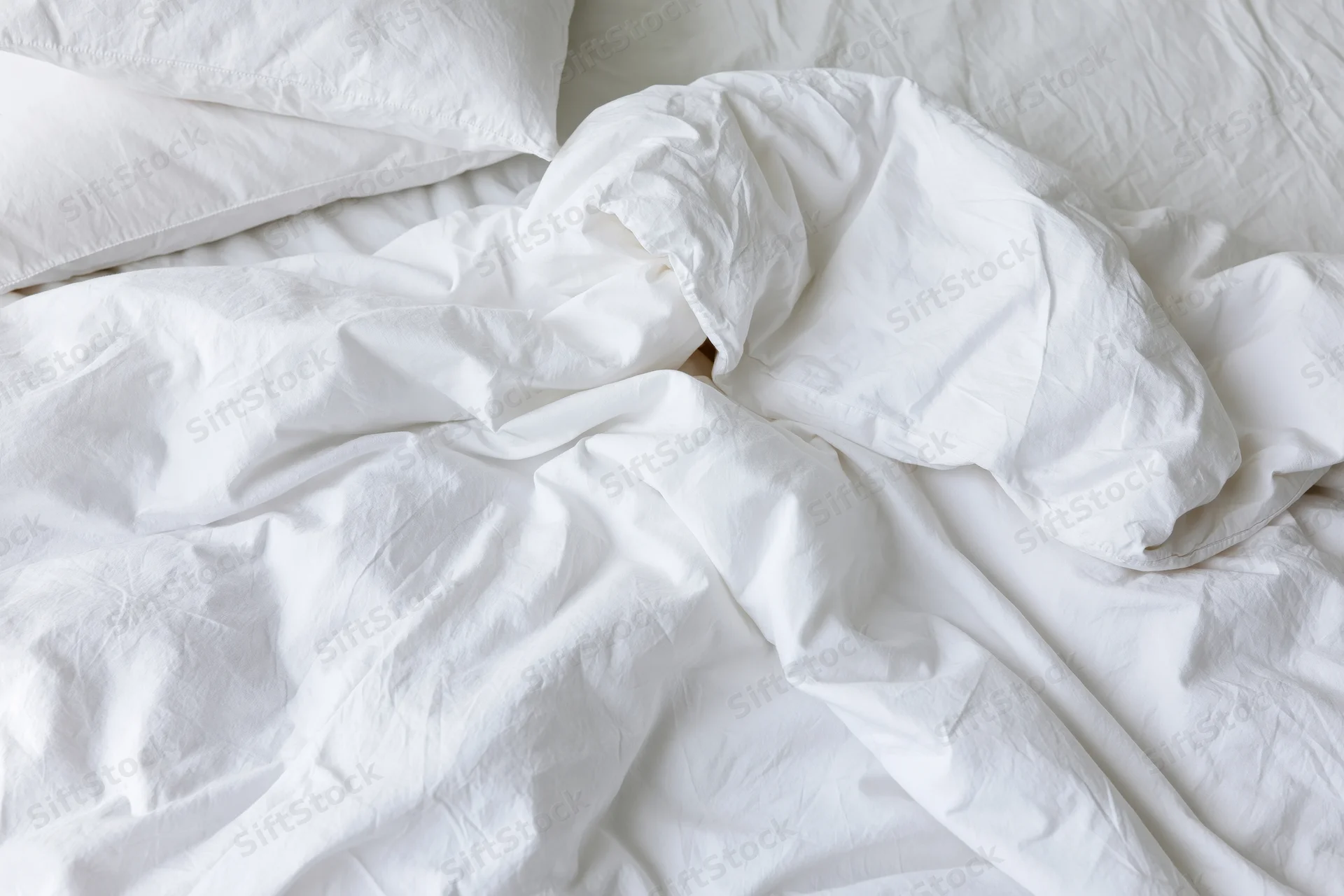 Unmade bed with rumpled white cotton duvet and two pillows in bedroom