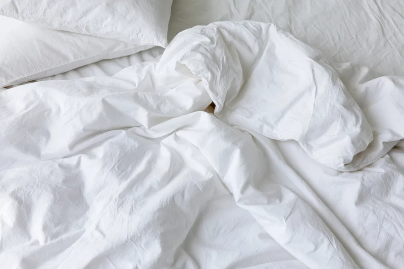Unmade bed with rumpled white cotton duvet and two pillows in bedroom