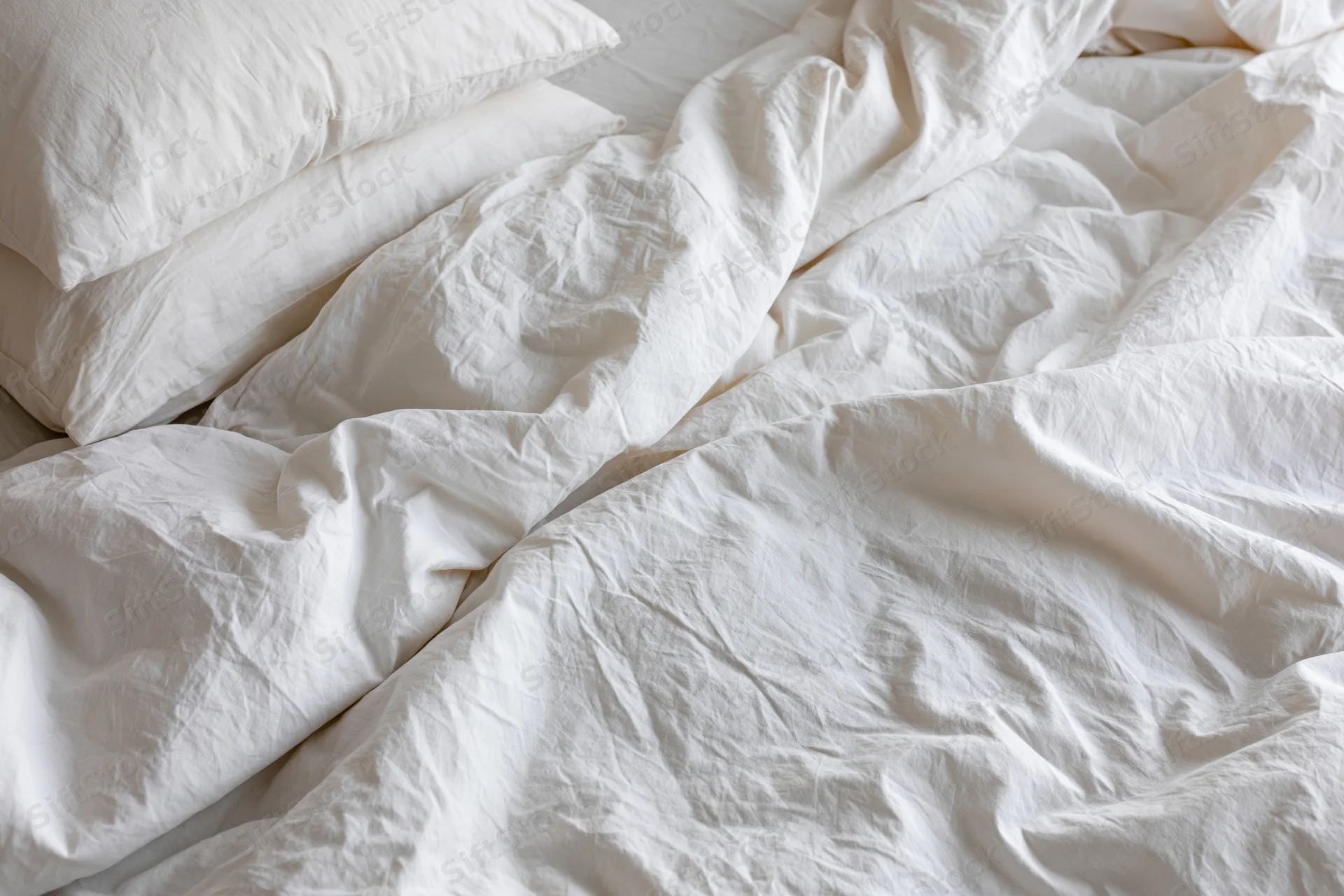 Unmade bed with rumpled white cotton duvet and two pillows in bedroom