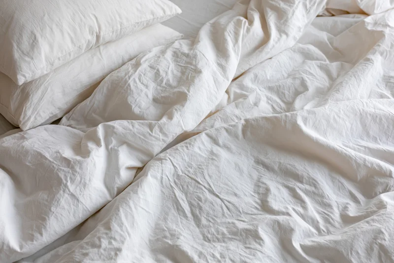 Unmade bed with rumpled white cotton duvet and two pillows in bedroom