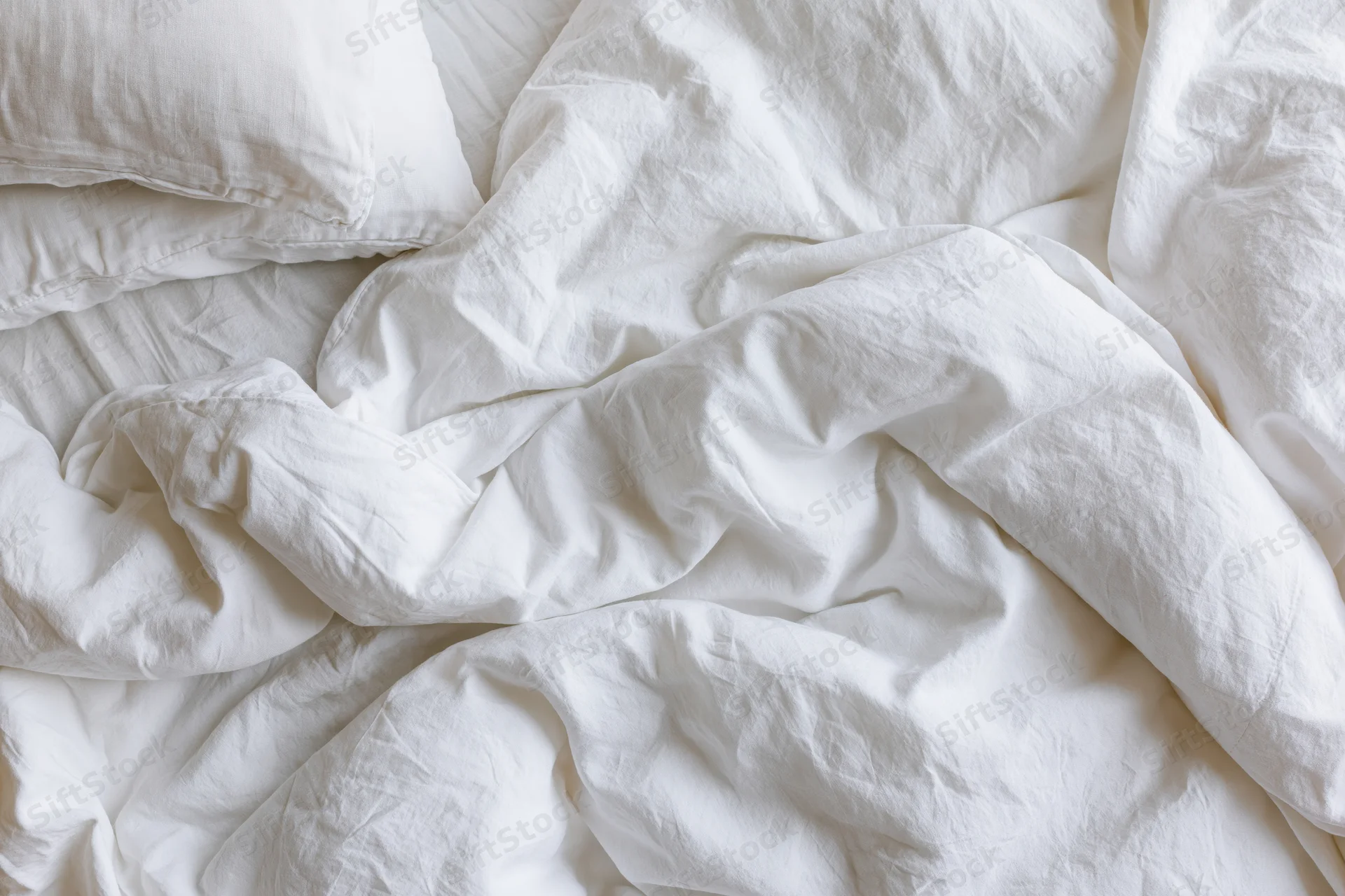 Unmade bed with rumpled white cotton duvet and two pillows in bedroom