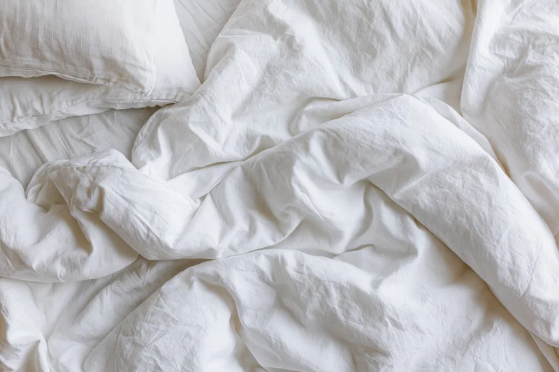 Unmade bed with rumpled white cotton duvet and two pillows in bedroom