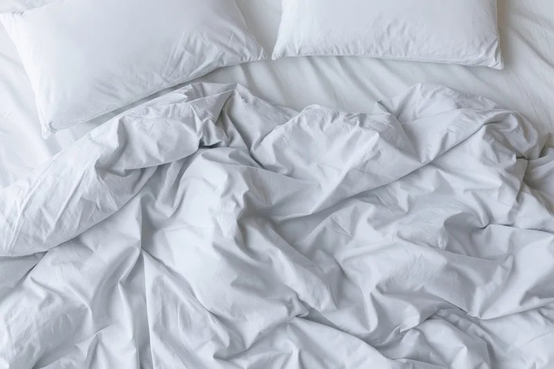 Unmade bed with crumpled white duvet and two flat pillows viewed from above