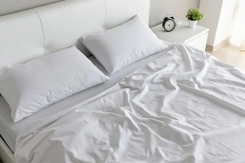 Unmade bed with white rumpled cotton sheets and two pillows in a bright modern bedroom