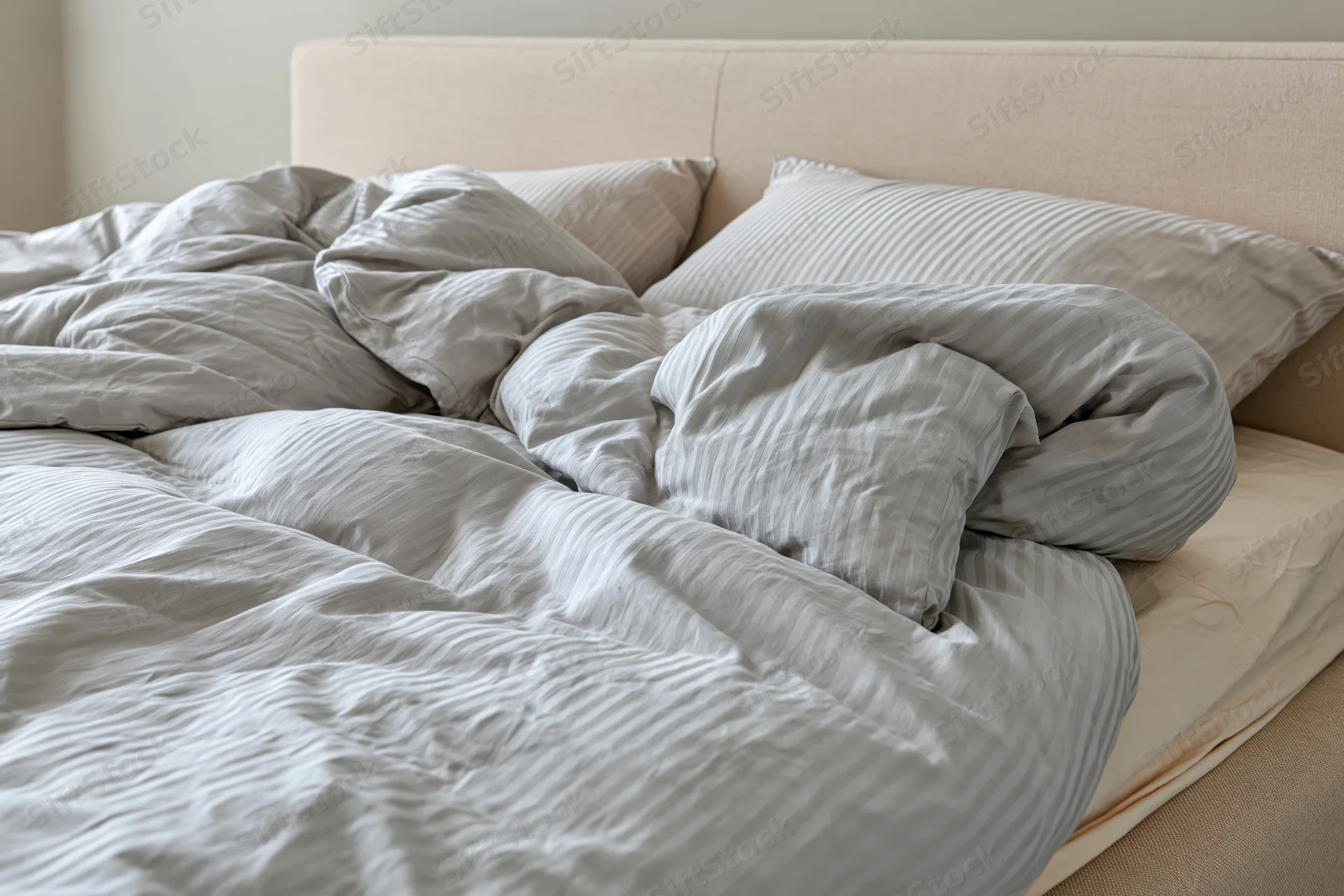 Unmade double bed with rumpled duvet and scattered pillows in bedroom
