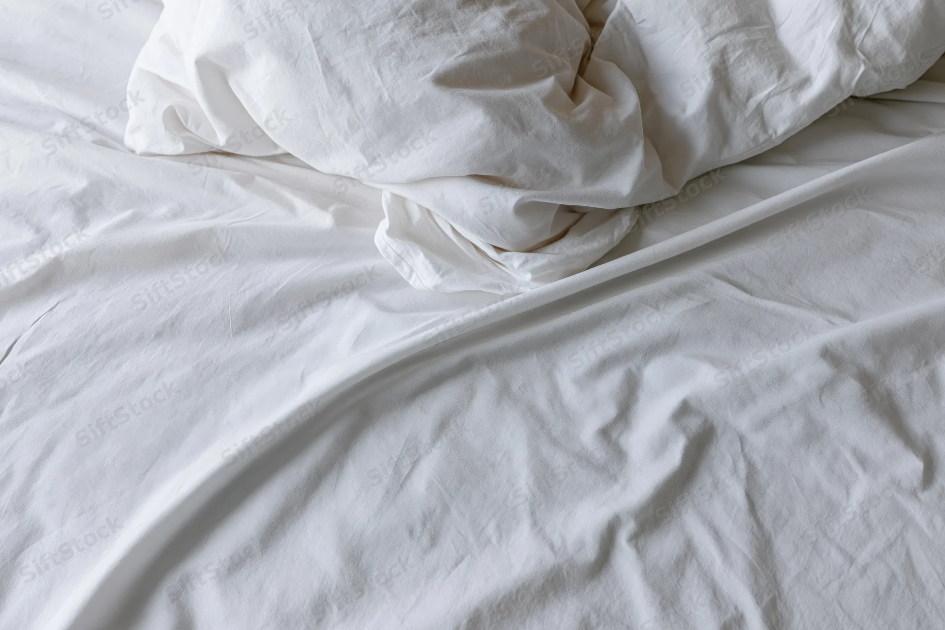 Unmade bed with crumpled white duvet and pillow mound in a hotel room