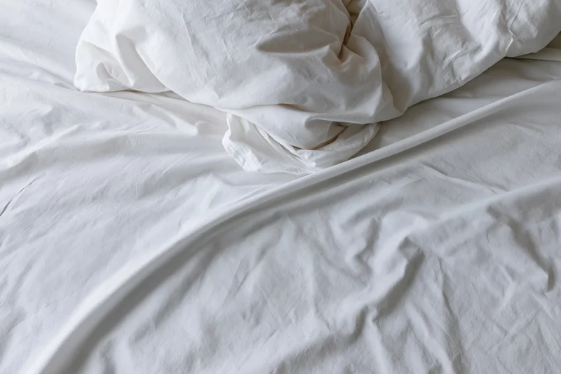 Unmade bed with crumpled white duvet and pillow mound in a hotel room