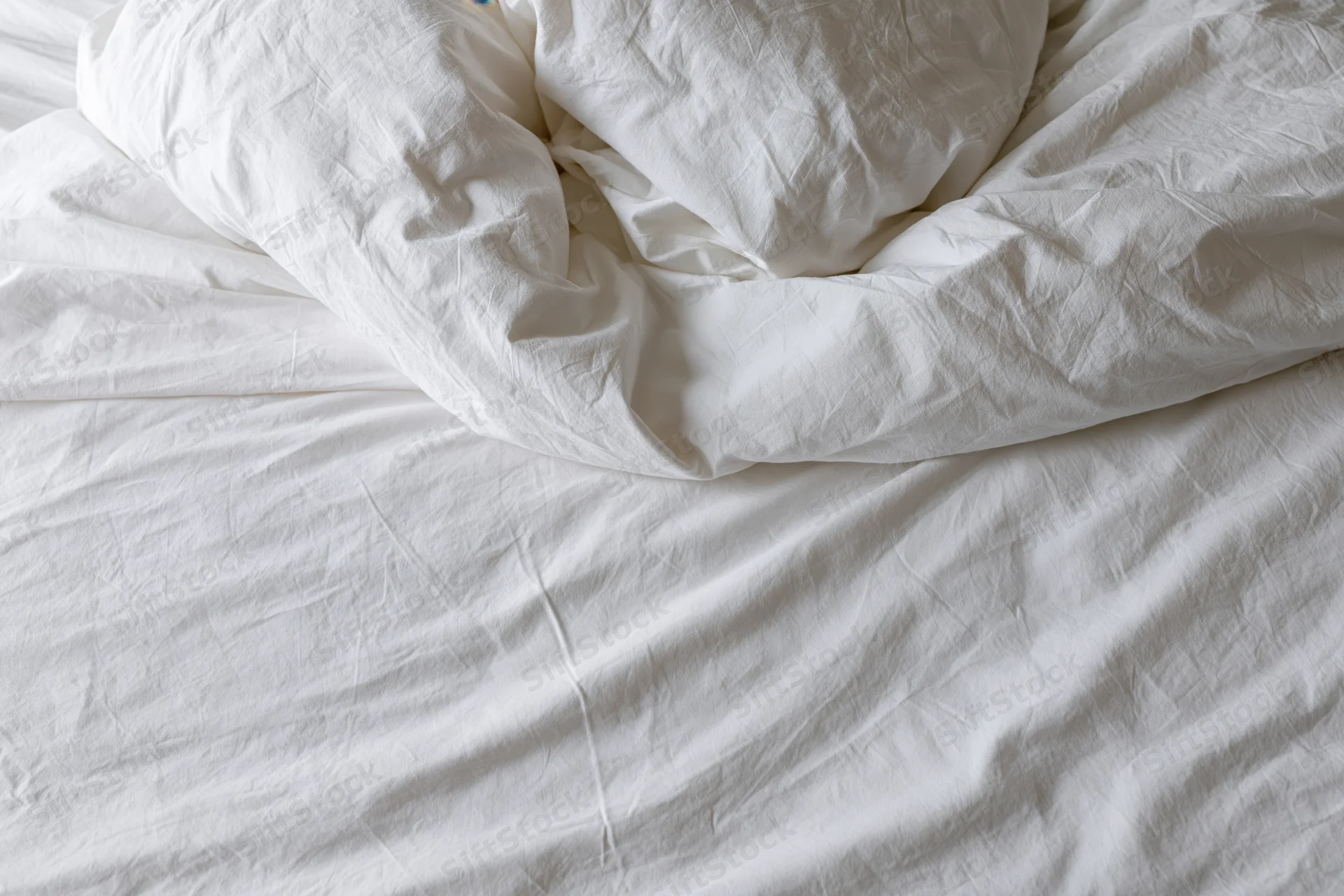 Unmade bed with crumpled white duvet and pillow mound in a hotel room