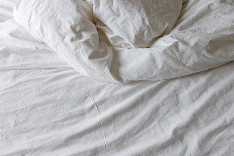 Unmade bed with crumpled white duvet and pillow mound in a hotel room