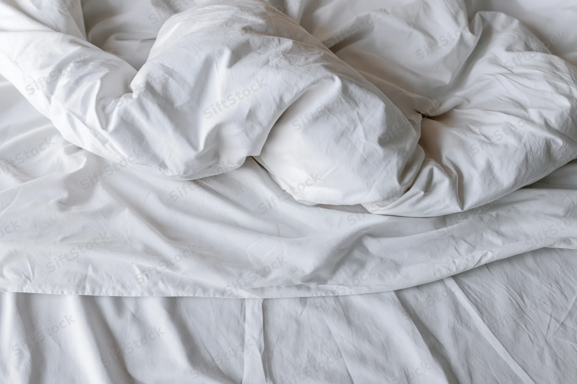 Unmade bed with crumpled white duvet and pillow mound in a hotel room