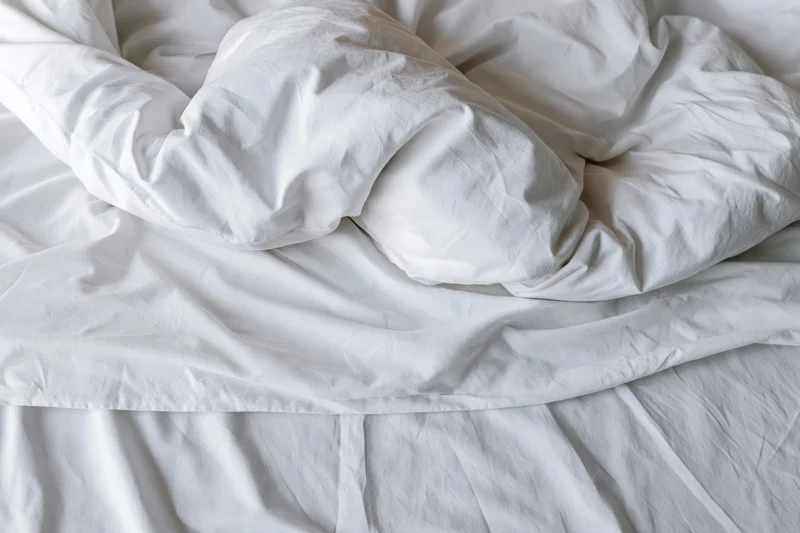 Unmade bed with crumpled white duvet and pillow mound in a hotel room