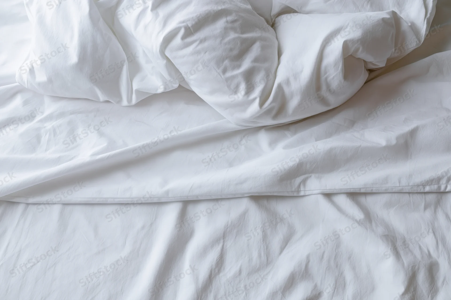 Unmade bed with crumpled white duvet and pillow mound in a hotel room