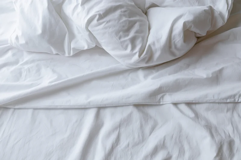 Unmade bed with crumpled white duvet and pillow mound in a hotel room