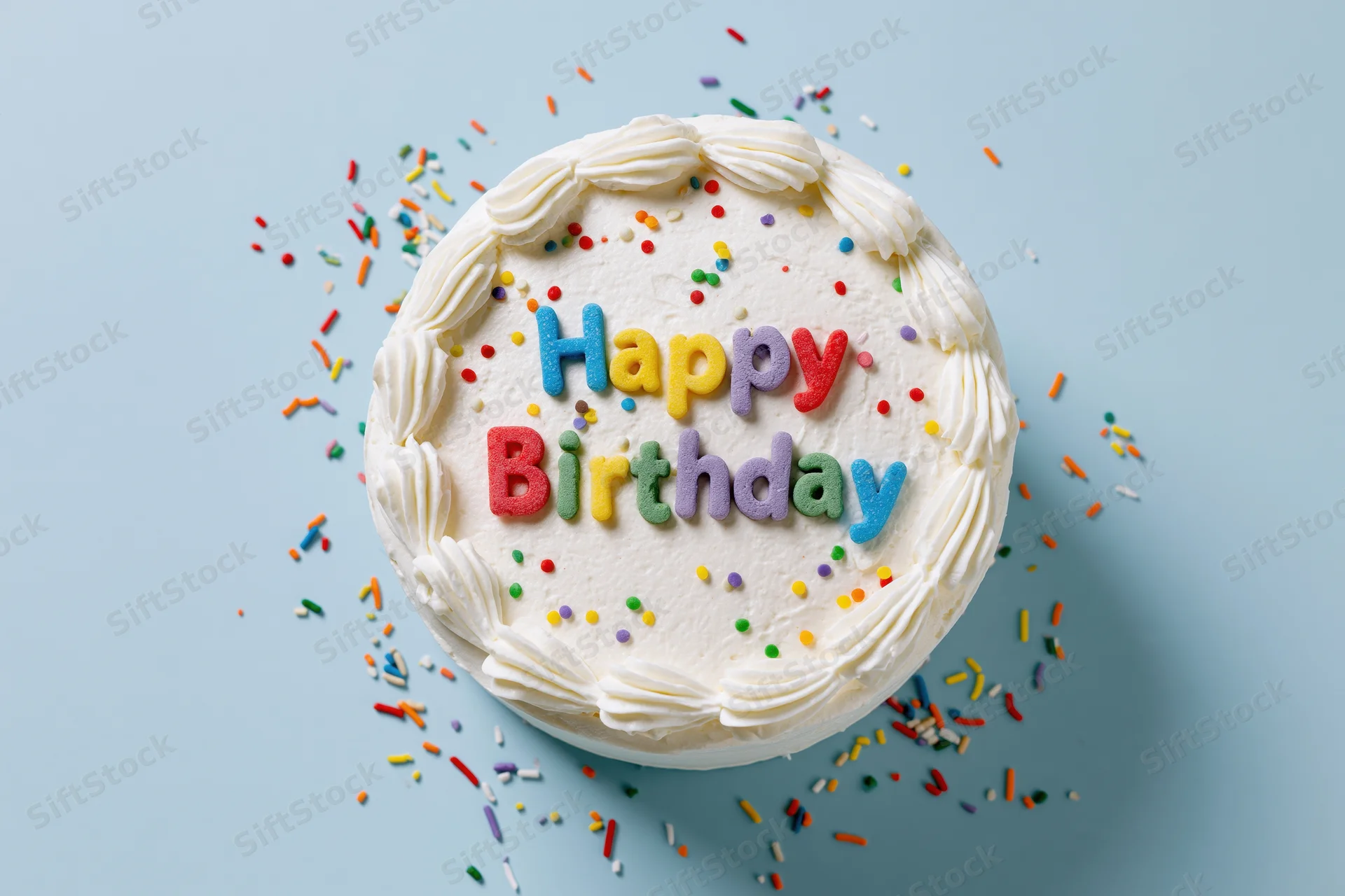 Round white-frosted birthday cake with colorful sprinkles and sugar letters spelling happy birthday on a light blue surface