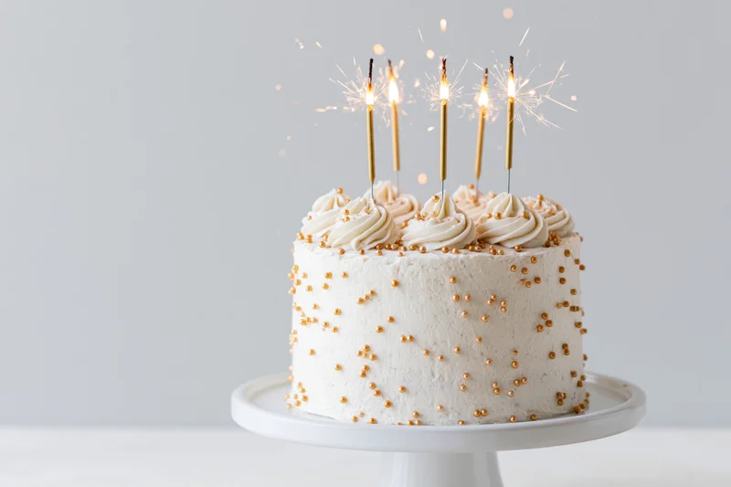 White celebration cake with lit sparklers on a white cake stand