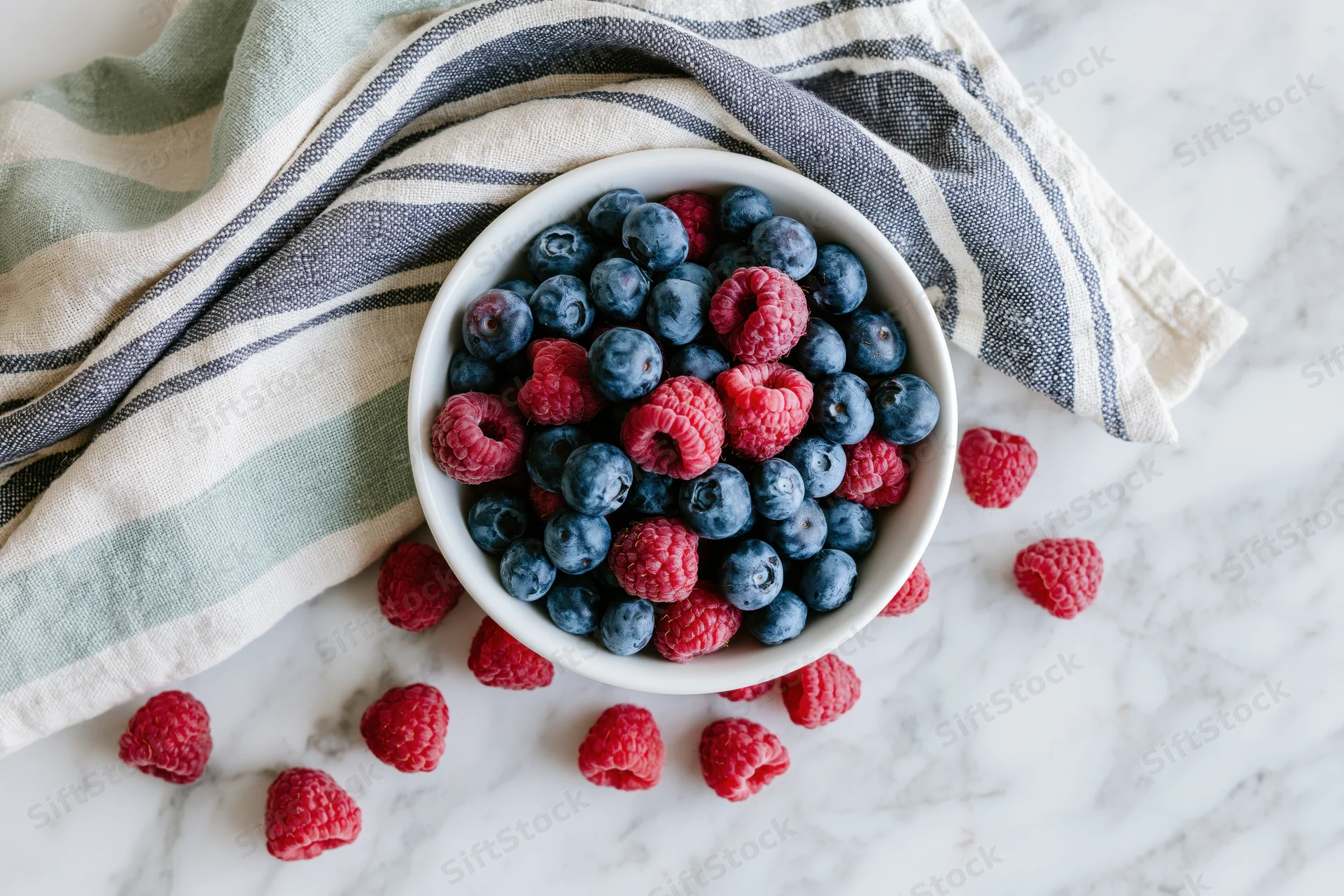 White ceramic bowl filled with blueberries and raspberries on marble countertop with striped cloth