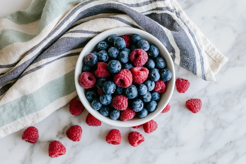 White ceramic bowl filled with blueberries and raspberries on marble countertop with striped cloth