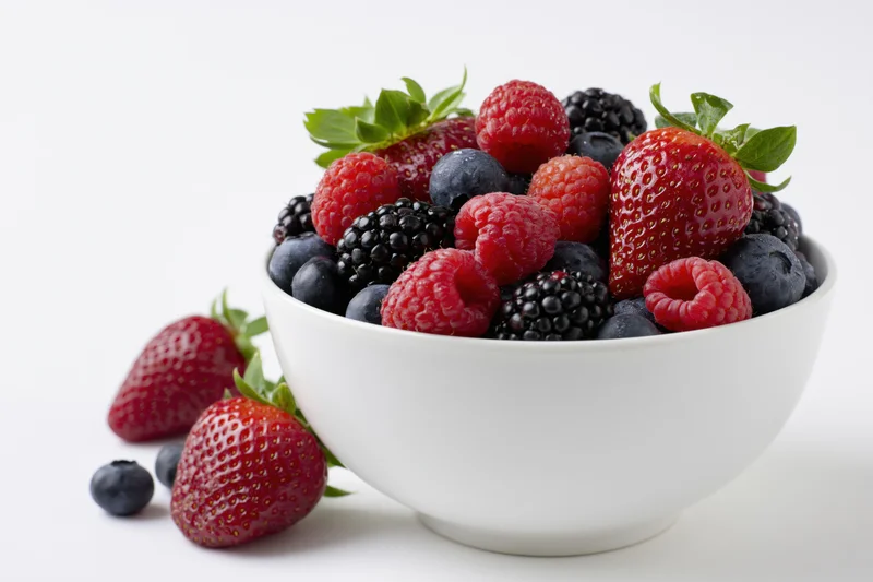 White ceramic bowl filled with fresh mixed berries on a plain white surface