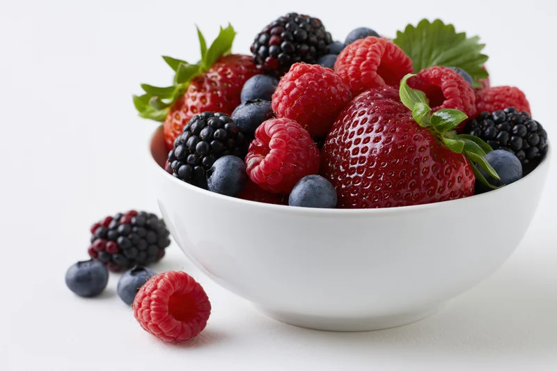 White ceramic bowl filled with fresh mixed berries including strawberries, raspberries, blueberries and blackberries on a plain white surface