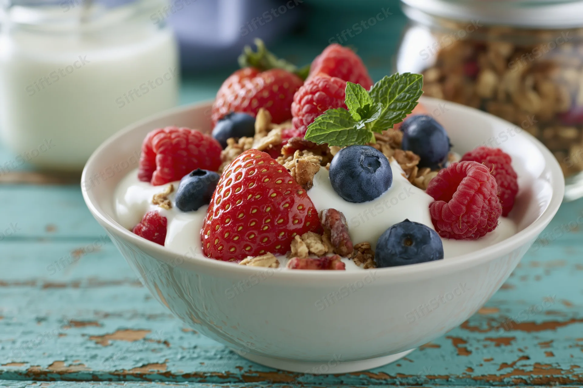 White ceramic bowl filled with yogurt granola and mixed berries on a turquoise wooden table