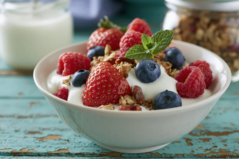 White ceramic bowl filled with yogurt granola and mixed berries on a turquoise wooden table
