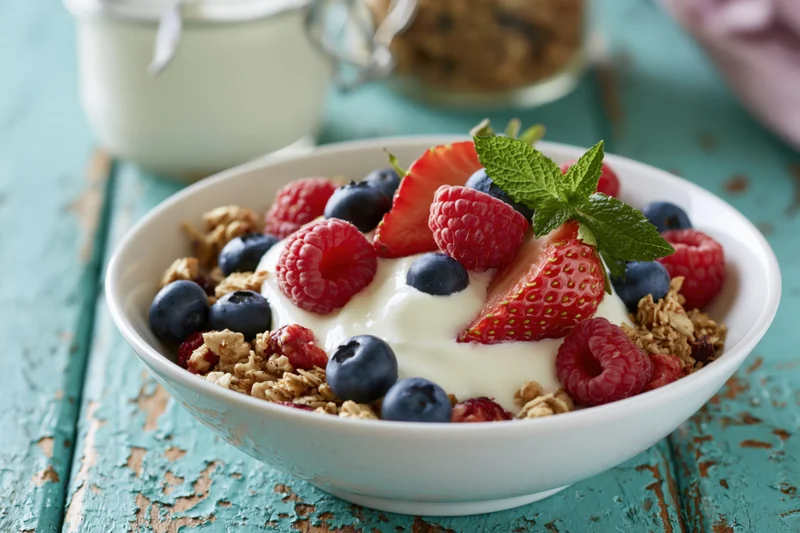 White ceramic bowl filled with granola, yogurt, and mixed berries on a turquoise wooden table