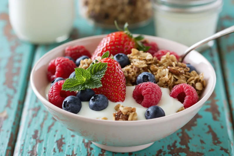 Ceramic bowl filled with yogurt, granola, and mixed berries on a turquoise wooden table