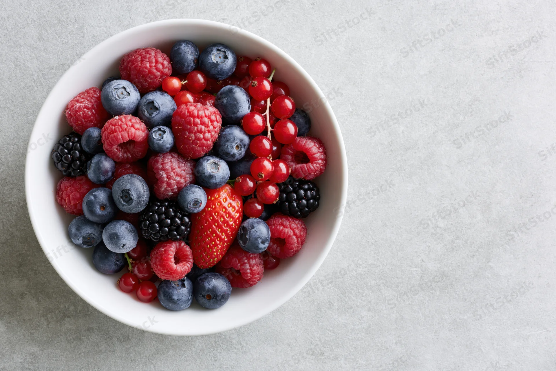 Mixed fresh berries in a white ceramic bowl on a gray surface