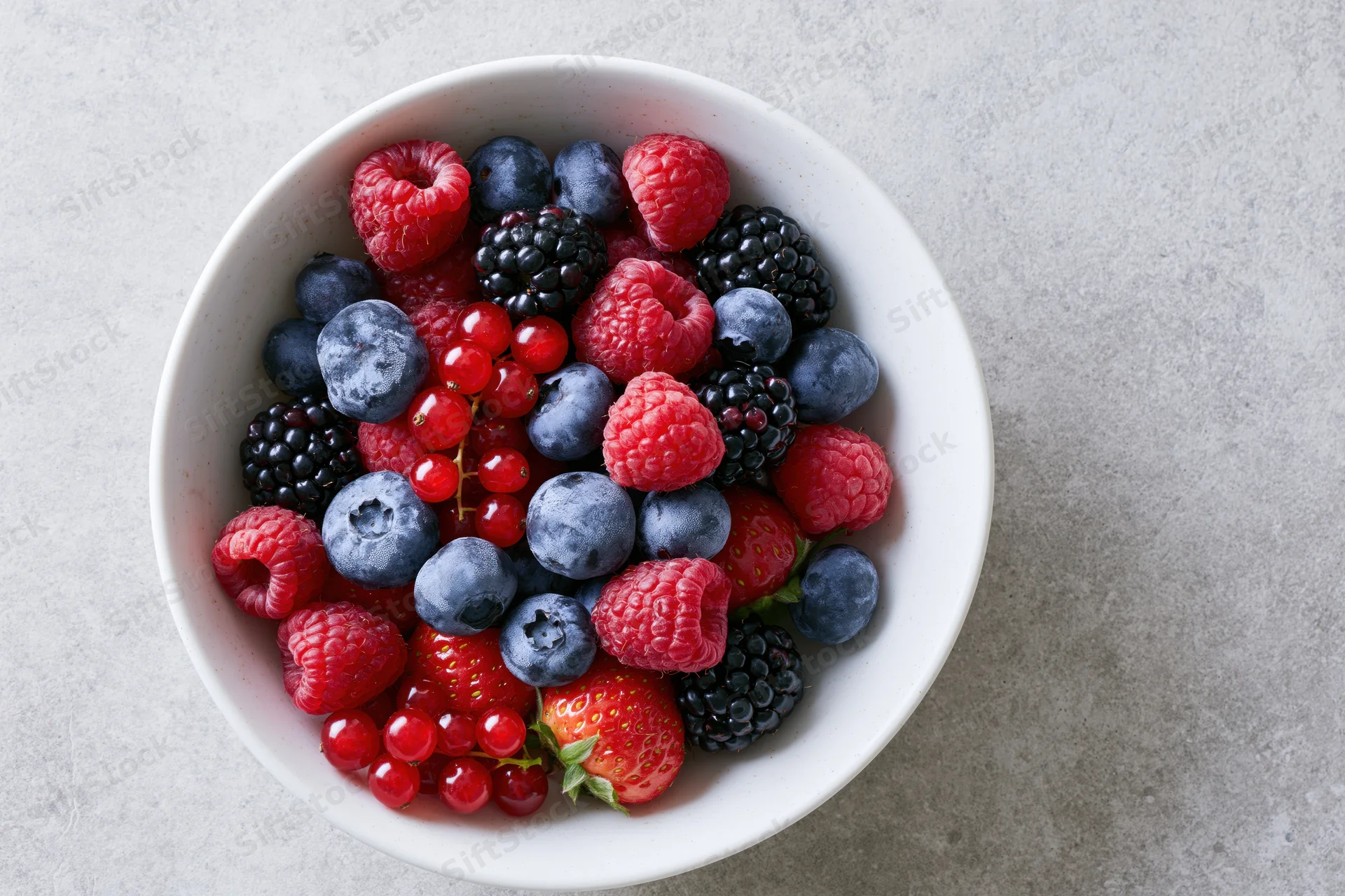 Mixed fresh berries in a white ceramic bowl on a gray surface