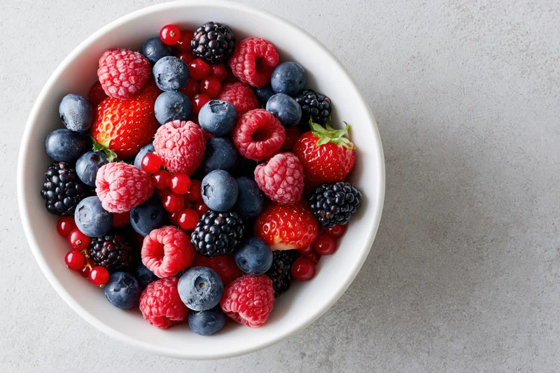 Mixed fresh berries in a white ceramic bowl on a light countertop, top view