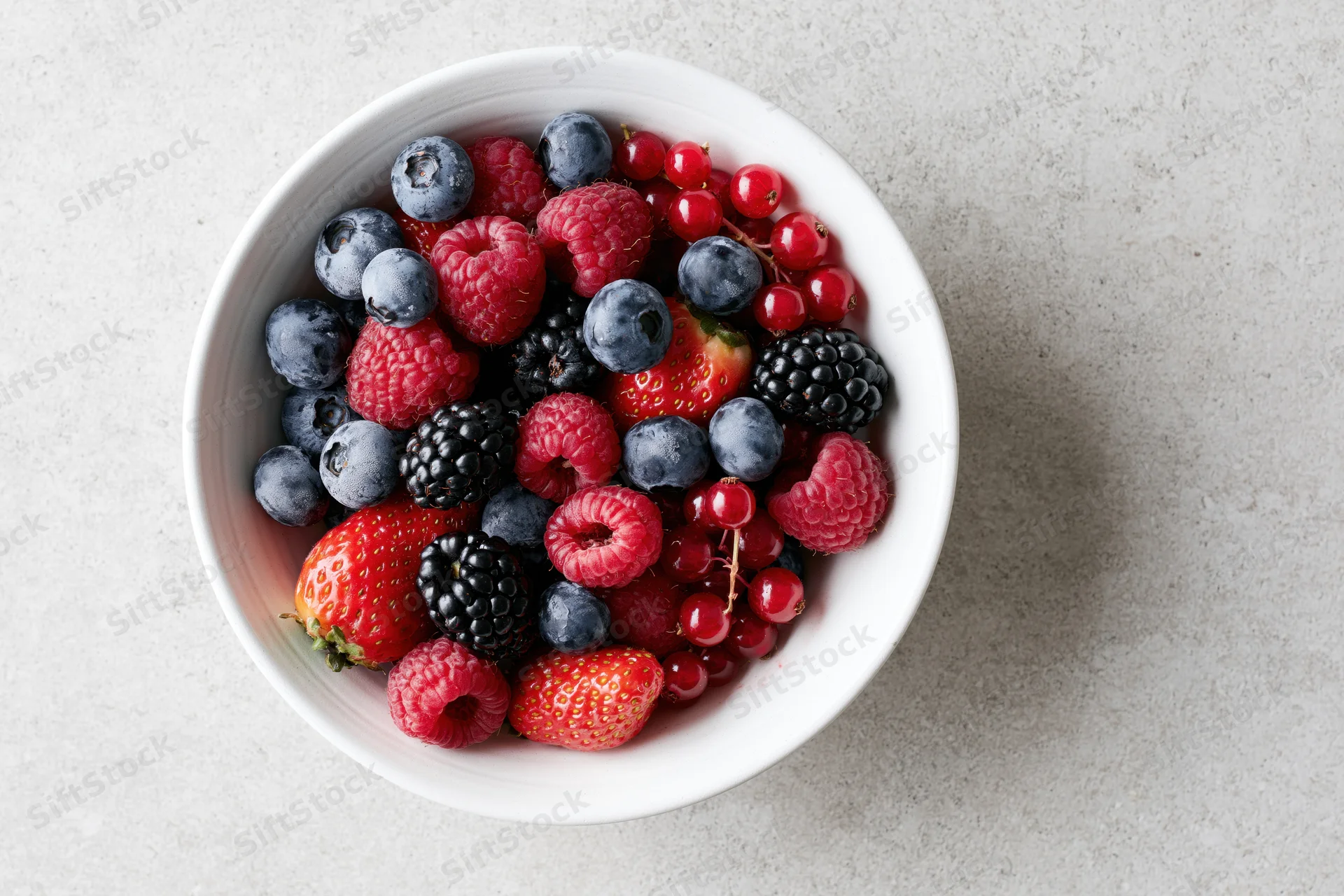 Mixed fresh berries in a white ceramic bowl on a gray countertop, top view