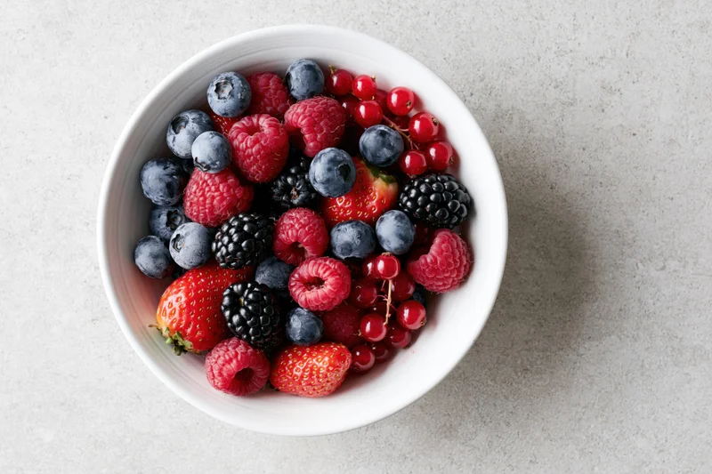 Mixed fresh berries in a white ceramic bowl on a gray countertop, top view