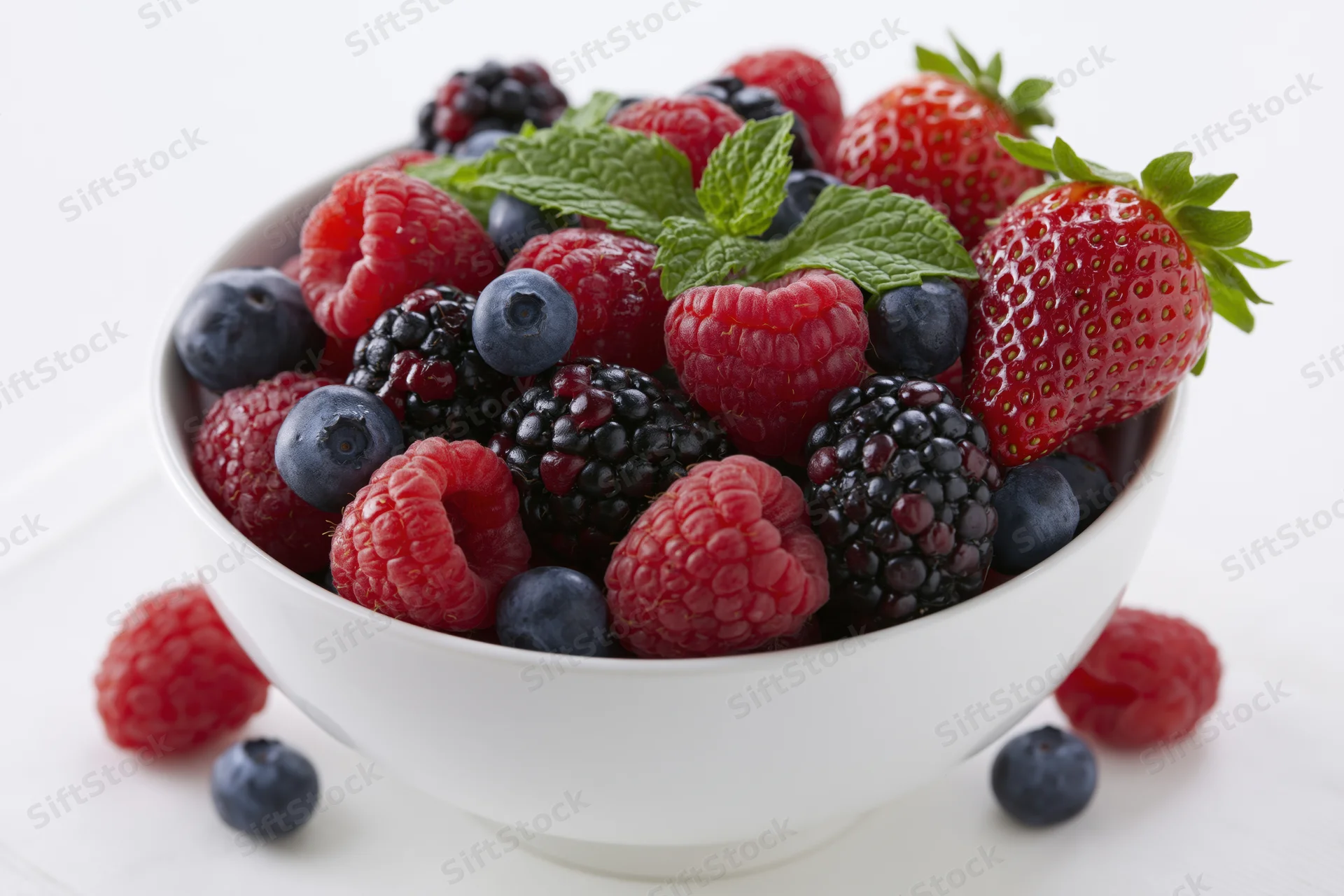 White ceramic bowl filled with mixed fresh berries and mint leaves on a white surface