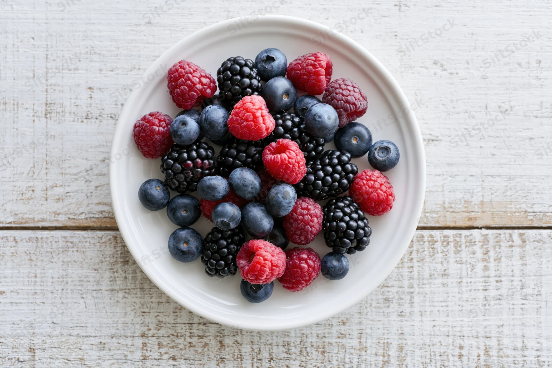 Mixed berries on a white ceramic plate on a wooden surface