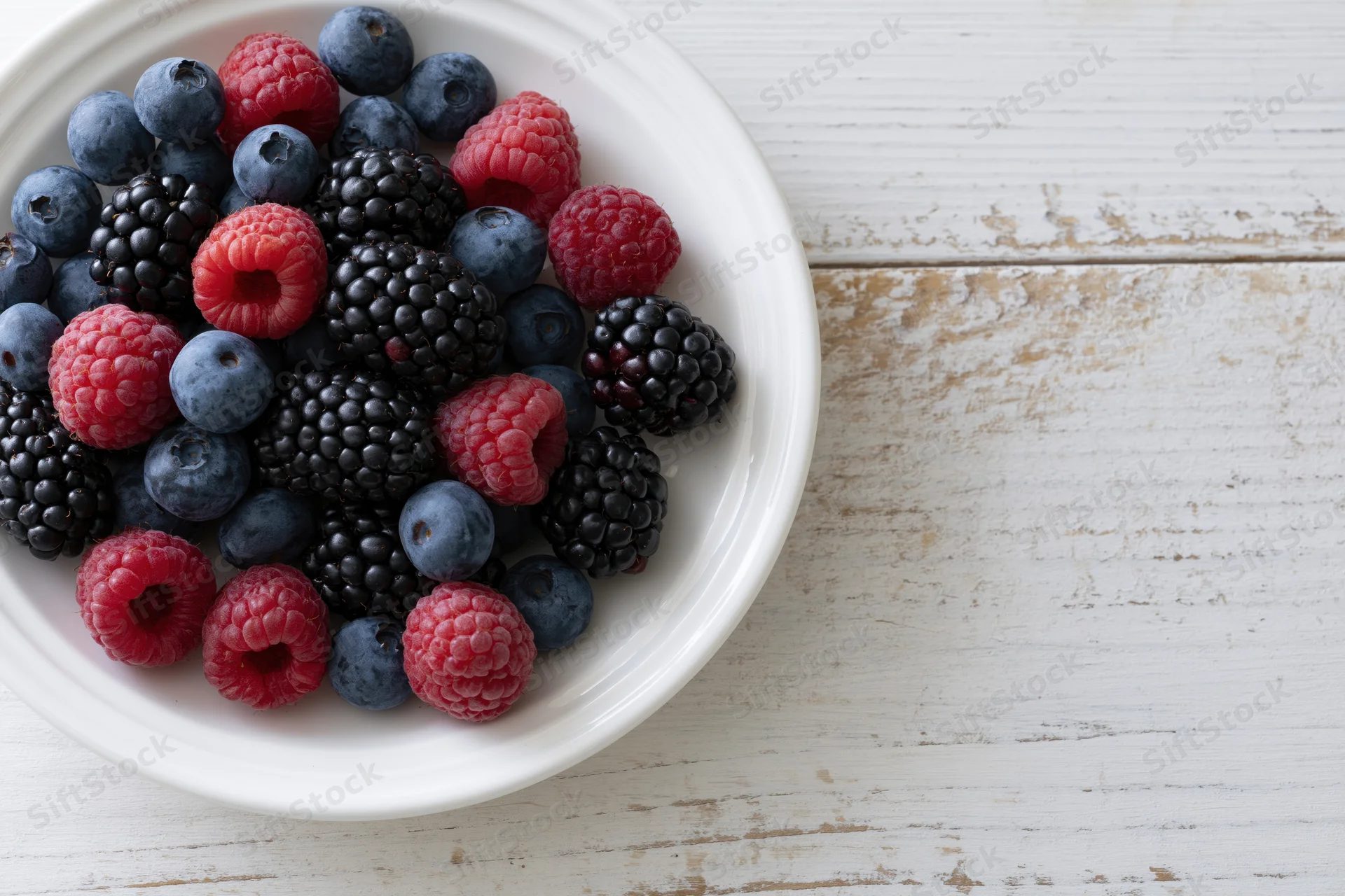 A white ceramic plate filled with blueberries, blackberries and raspberries on a rustic wooden table