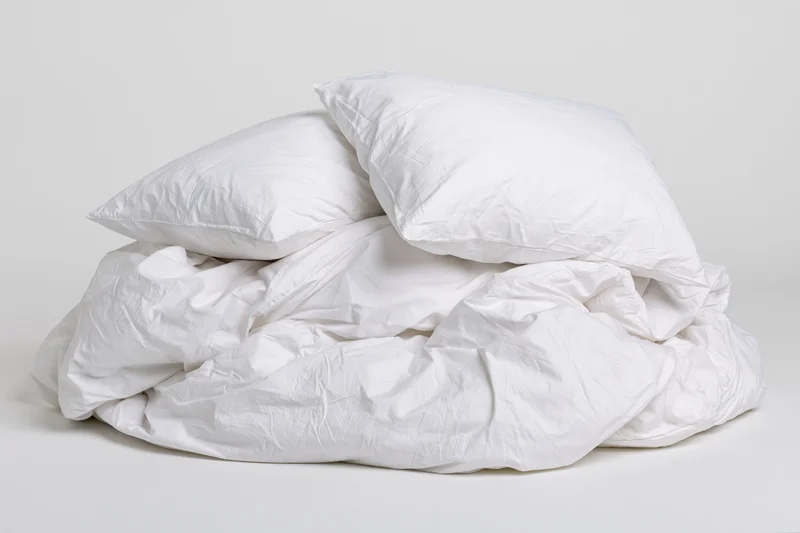 White cotton duvet and two pillows piled loosely on a plain surface