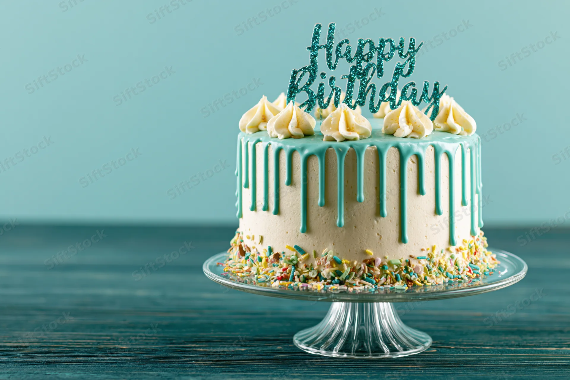 Birthday cake with teal drip frosting and sprinkles on a glass stand