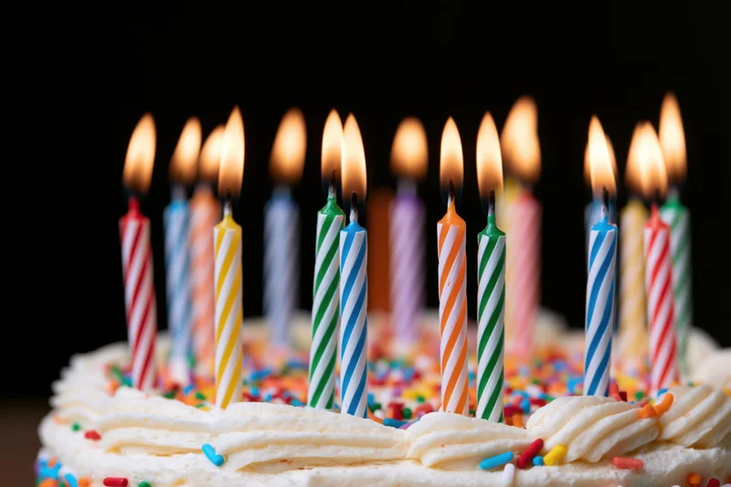White frosted birthday cake with lit striped candles and colorful sprinkles