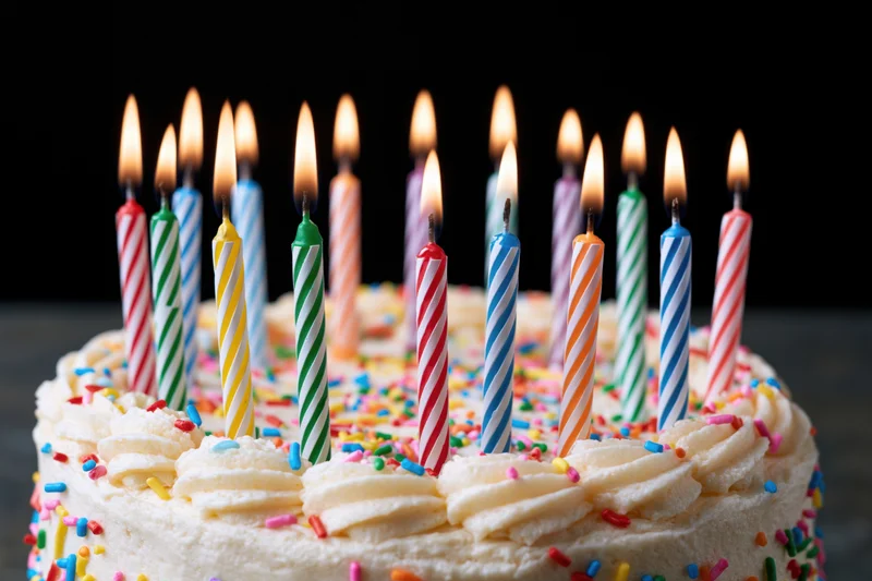 White birthday cake topped with a row of lit striped candles