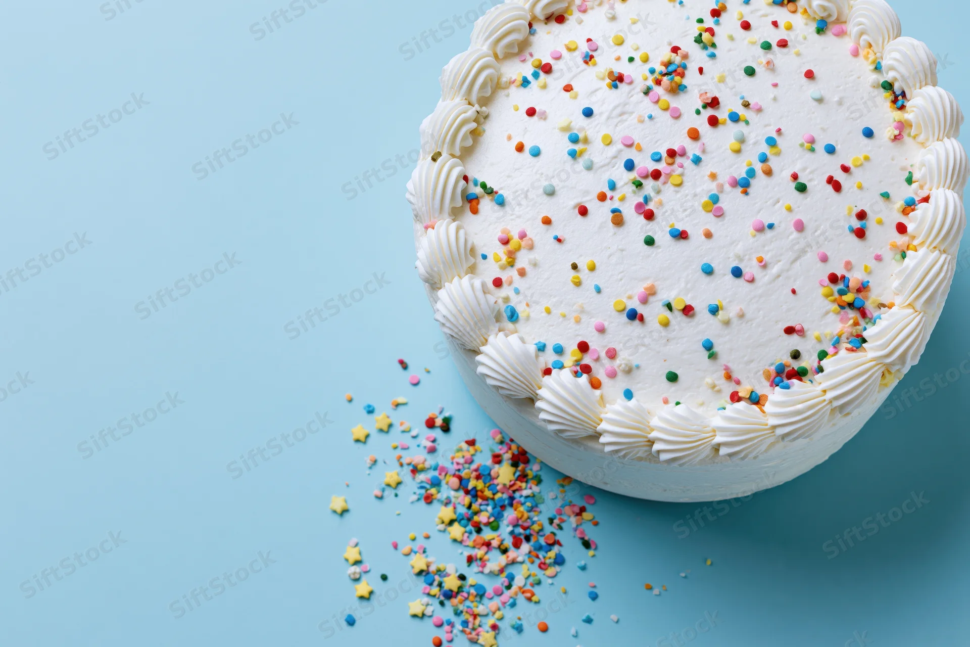 White frosted birthday cake with piped shell border and colorful sprinkles on blue surface