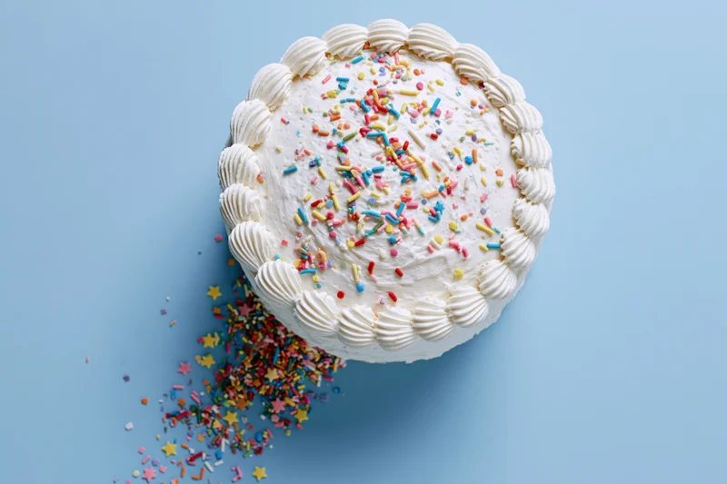 White frosted birthday cake with piped shell border and colorful sprinkles on blue background