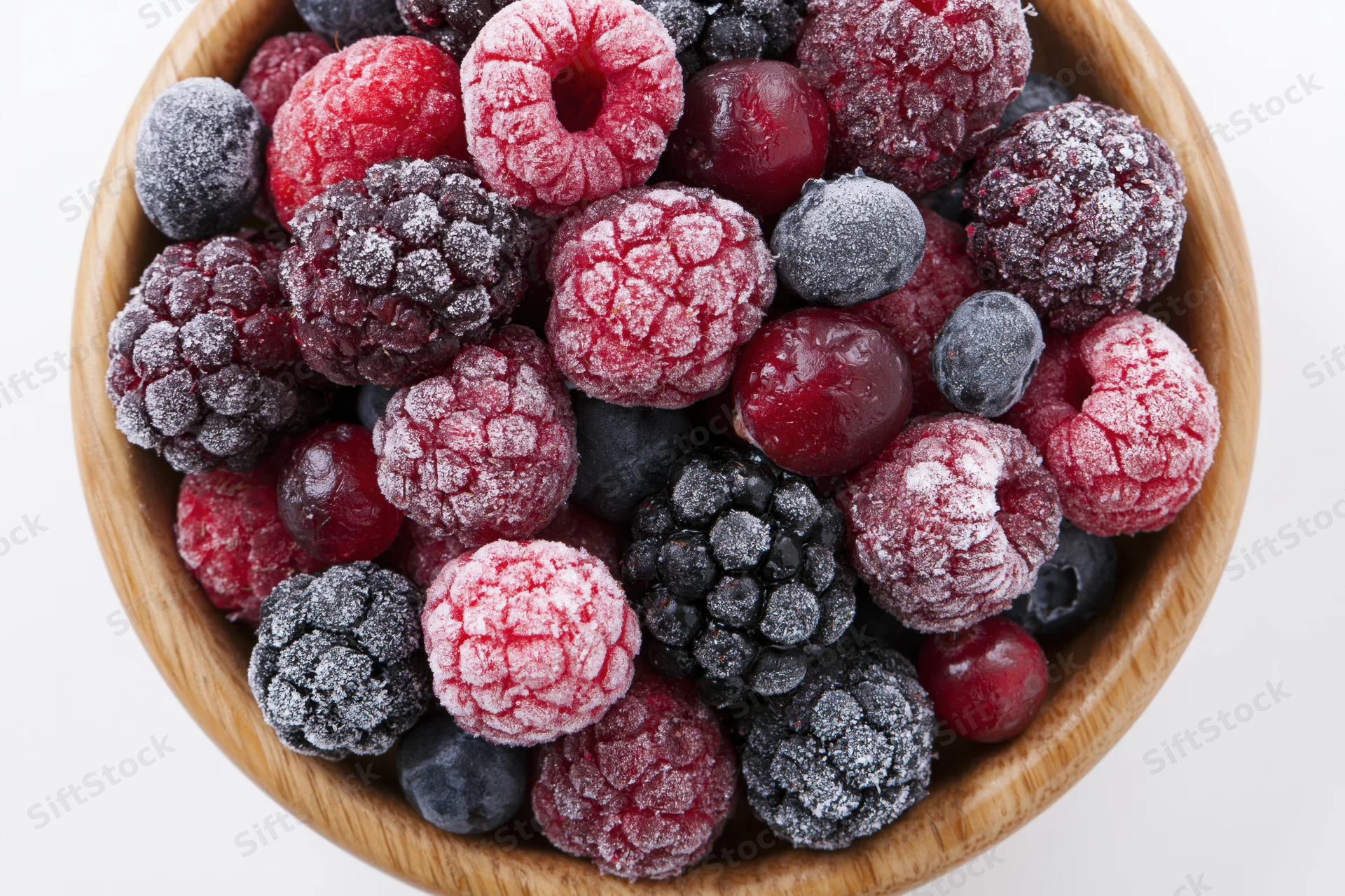 Frozen mixed berries in a wooden bowl viewed from above on white background