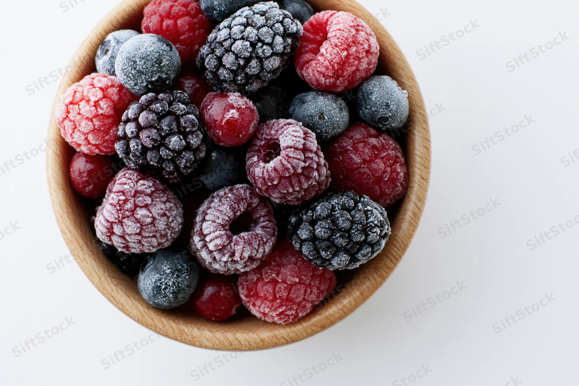 Frozen mixed berries in a wooden bowl on white background