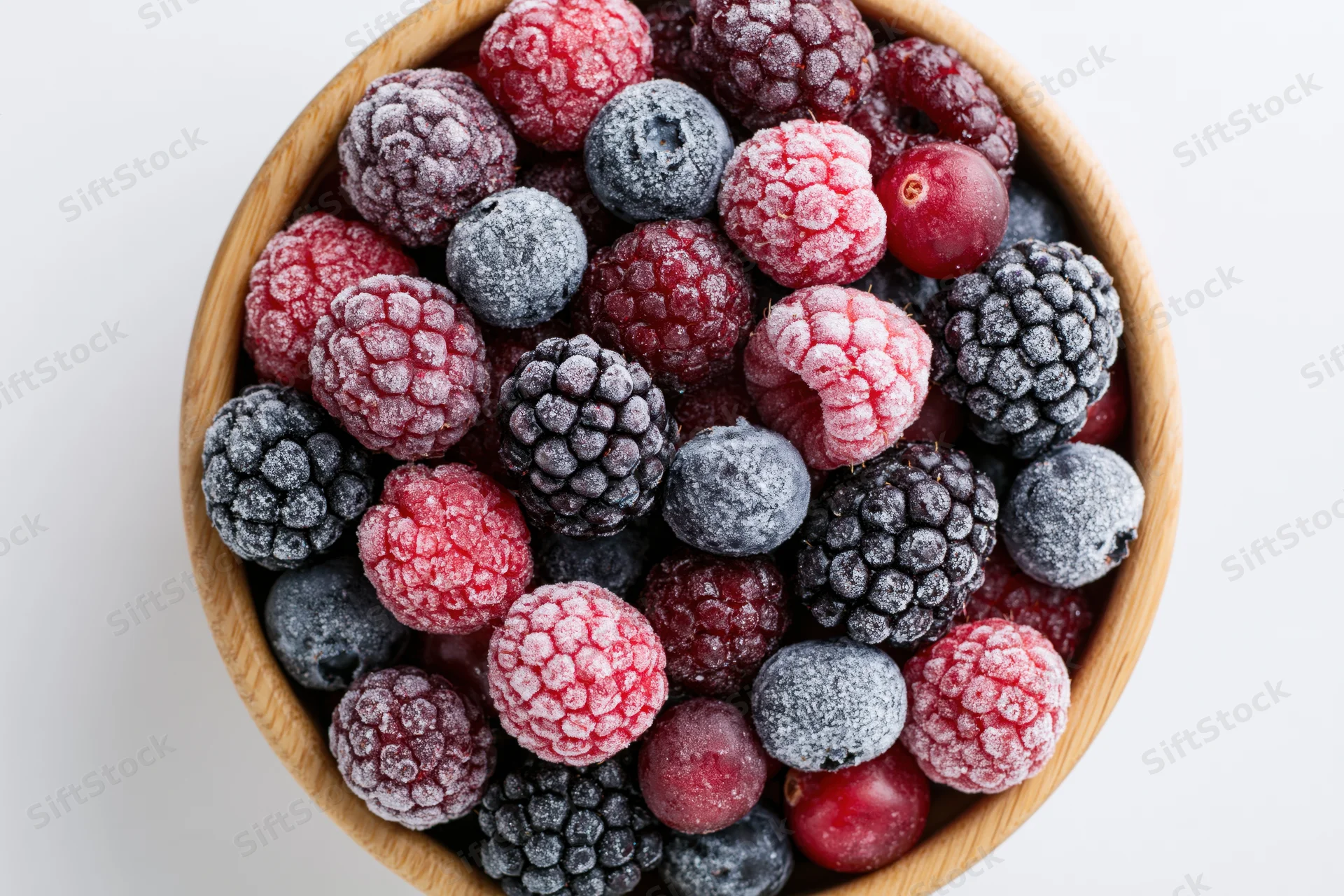 Mixed frozen berries in a wooden bowl viewed from above on white background